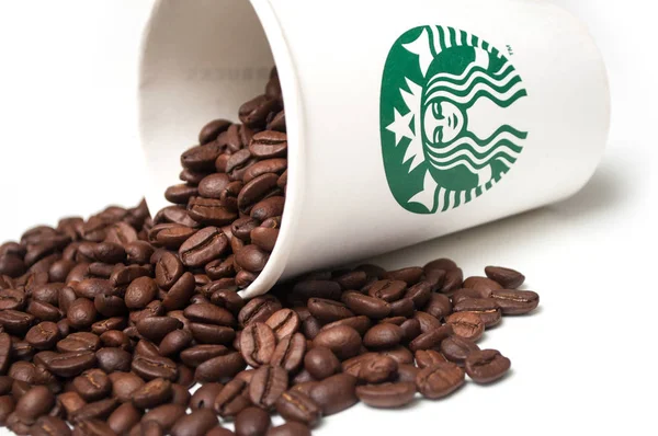 Grãos de café que caem de uma xícara de café Starbucks no fundo branco — Fotografia de Stock