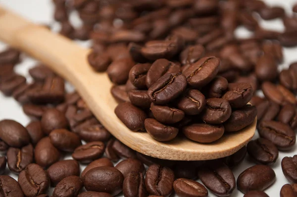 Fechar os grãos de café em uma colher de madeira no fundo branco — Fotografia de Stock