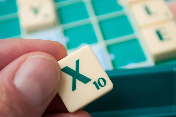 Plastic letters X in de hand op Scrabble bordspel — Stockfoto