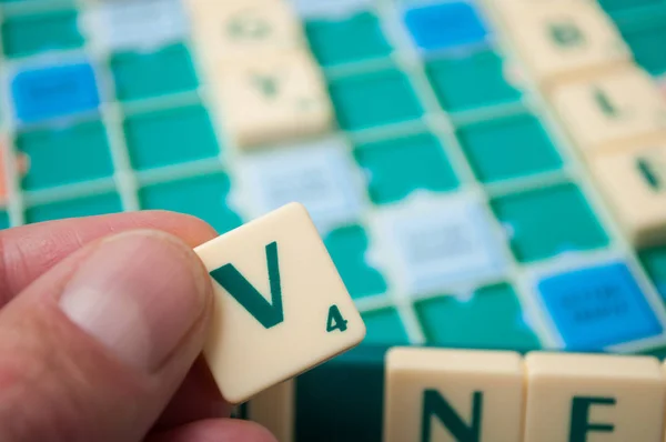 Plastic letters V in hand on Scrabble board game — Stock Photo, Image