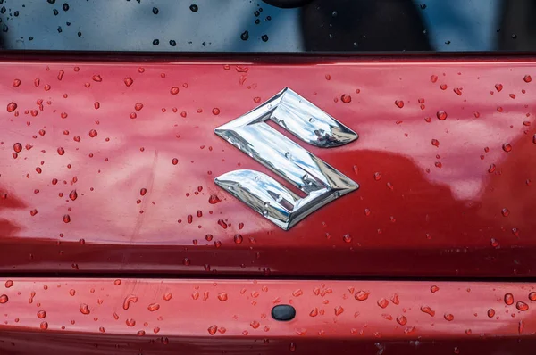 Rain drops on Suzuki logo on rear car parked in the street — Stock Photo, Image