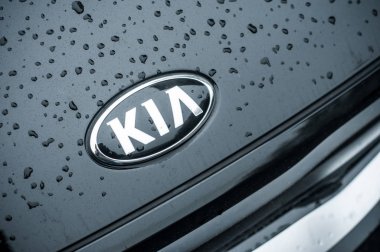 Kia logosu üzerine yağmur damlaları. Siyah arabanın önüne park edilmiş.