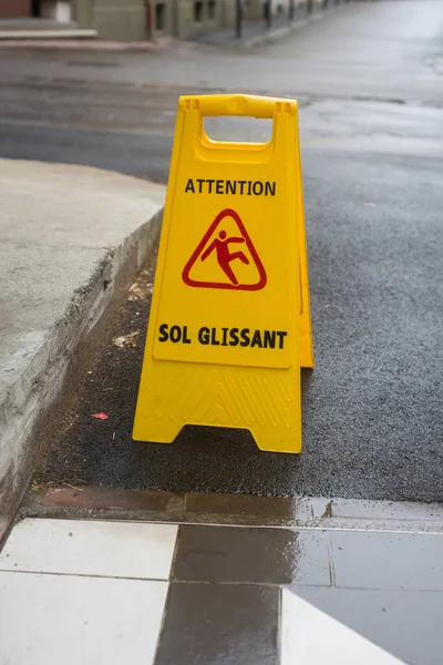 Closeup of wet floor sign on yellow plastic board , with text in french, attention sol glissant, traduction in english, Attention wet floor