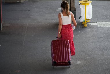 Arka planda, tren istasyonunda kırmızı bavulla yürüyen kadının portresi var.