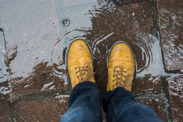 通りの水の水たまりに立っている革のブーツを着た男の足の閉鎖 — ストック写真