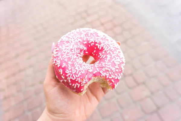 Mordido donut rosa na mão. donut com uma cobertura de chocolate rosa . — Fotografia de Stock