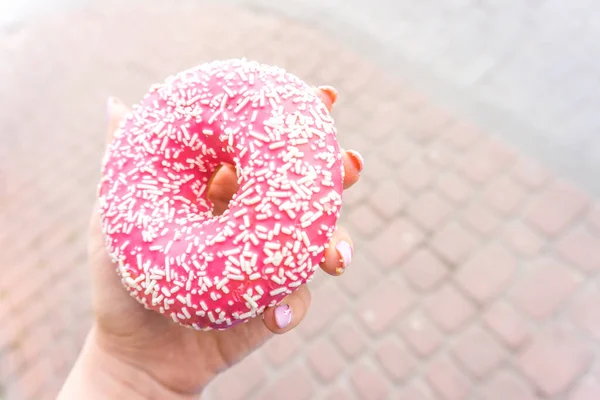 Sweet pink and white doughnut in womans hand with copy space.