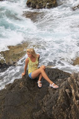 Kız denizde kayaların üzerinde oturup Karadağ sahilindeki Mogren Budva 'nın azgın dalgalarını seyrediyor.. 