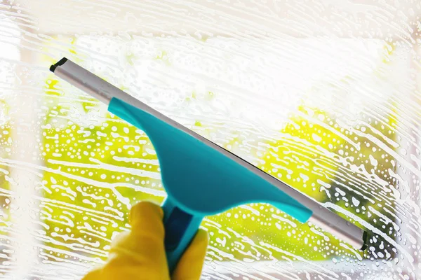 Sabunlu bir pencere ile kauçuk squeegee . Yeşil bokeh arka plan ile yıkama pencereleri.