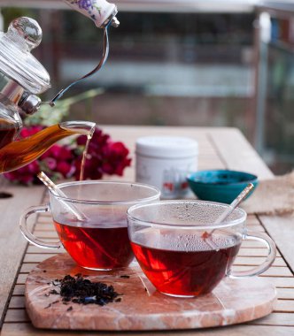 Çiçekli ahşap bir masa üzerinde fincanlara çay dökülüyor.