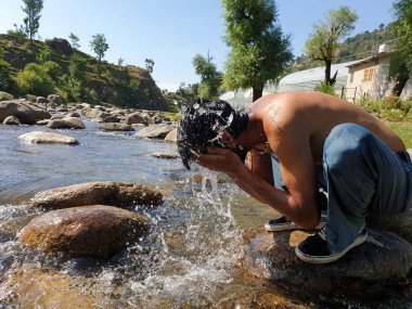 Nehirde yüzünü yıkayan üstsüz bir adamın fotoğrafı, Hintli bir adamın yüzünü doğada suyla yıkaması.