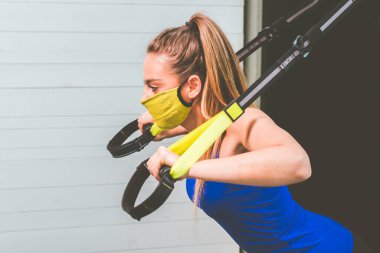 Kollarını koruyucu maskeyle çalıştıran ve salgın hastalık salgını sırasında spor salonunda Trx Fitness 'ı bağlayan bir kız 19 yaşında şınav çeken bir kadın göğüs üst göğüs kasları kaslarını çalıştırıyor.