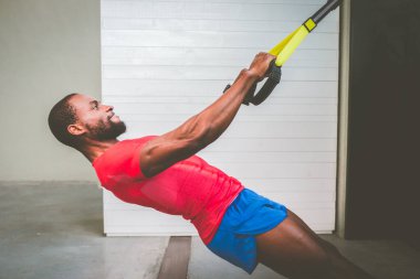 Spor salonunda trx fitness kayışlarıyla antrenman yapan genç siyah antrenör - çekici Afro-Amerikan adam spor salonunda trx fitness kayışlarıyla Crossfit şınav çekiyor