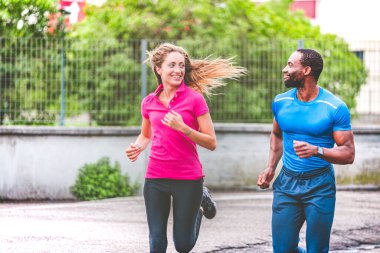 Sokakta koşarken birbirlerine gülümseyen genç bir çift. Afro-Amerikalı bir adam ve spor giysili güzel sarışın bir kız şehrin sokaklarında birlikte koşuyorlar.