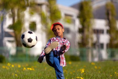 Küçük çocuk kaleye ateş ediyor. Genç Afro-Amerikan futbolcu çimlerin üzerinde futbol topunu tekmeliyor..