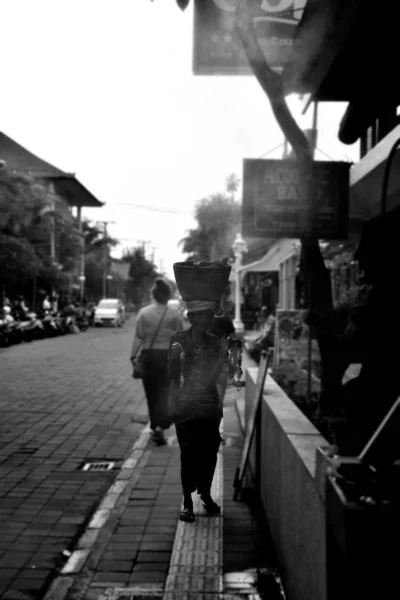 Vrouw is wandelen en het dragen van een mand op haar hoofd op de straat van Ubud in Bali. Zwart-wit fotografie uit Indonesië. — Stockfoto