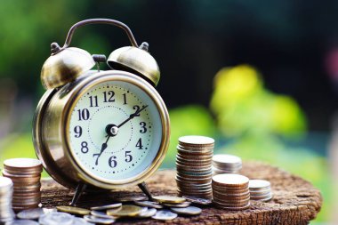 Çalar saat ve para yığınları ile ahşap masa üzerinde bulanıklık yeşil bahçe renkli, parlak sabah renk tonu, finans ve iş kavramı, kopya alanı