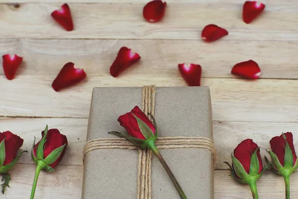 Eco friendly brown paper wrapped gift box present decorated with rose and other flowers on wooden background, valentine ornamental concept, copy space