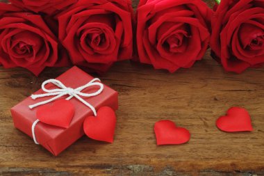 Çok güzel çiçek kırmızı renk gül çiçek ve ahşap masa arka planda mini kırmızı kalp figürü, tatlı Sevgililer günü hediyesi kavramı, kopya alanı ile dekore edilmiş zarif hediye kutusu