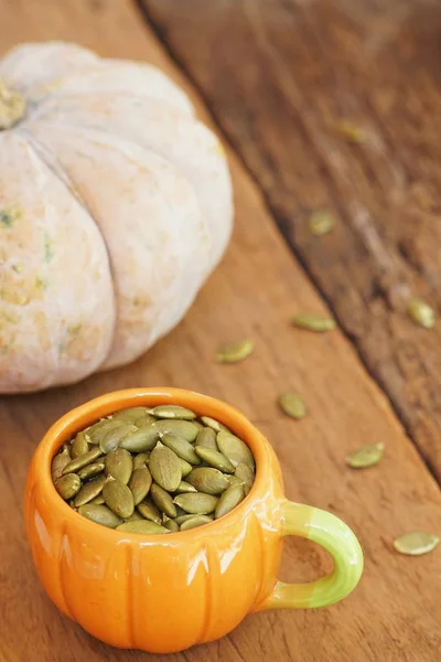 Pumpkin seed in pumpkin cup and fresh pumpkin fruit on classic wooden table background, copy space