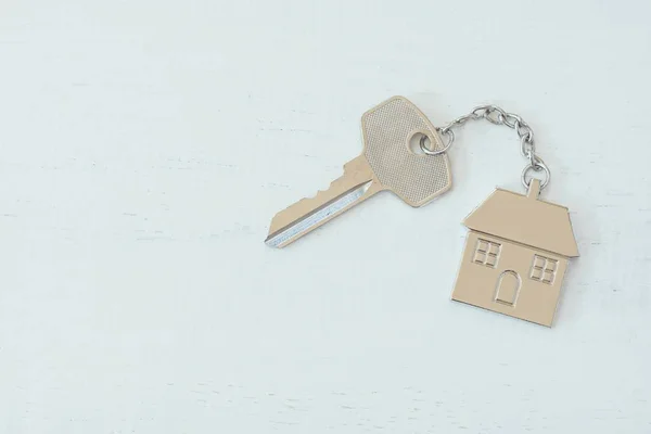 Home key with house keyring on white wood table background, property concept, copy space