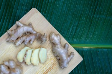 Taze zencefil kökü ve ahşap masa arka planda, sağlıklı Asya bitki kavramı, yaprak yeşil zemin üzerine dilimlenmiş zencefil alanı Kopyala