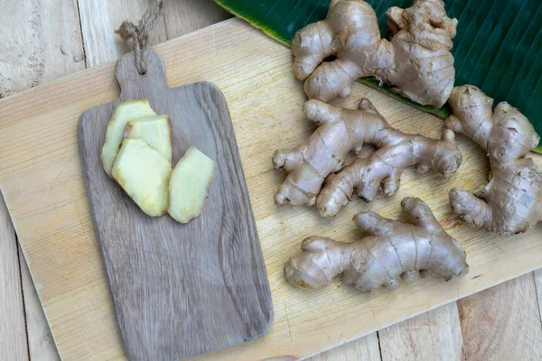 Fresh ginger root and ginger sliced on green leaf background on wood table background, healthy Asian herb concept, copy space