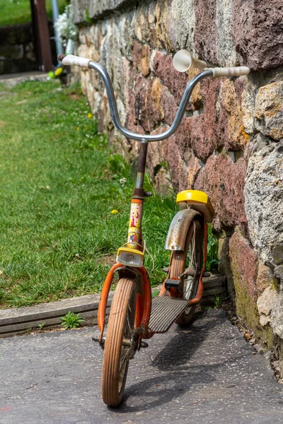 一辆用青草和石墙做后背的老橙色老式踢踏车 复古推动式摩托车 — 图库照片