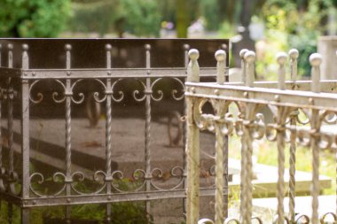 Mezarlıktaki siyah granit mezar taşının etrafındaki demir parmaklıkların yansıması..