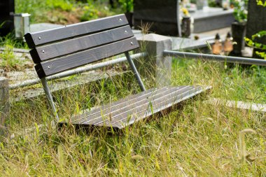 Metal kollu ahşap bankta mezarlıktaki çimlerin arasında duruyor. Huzurlu bir yer..