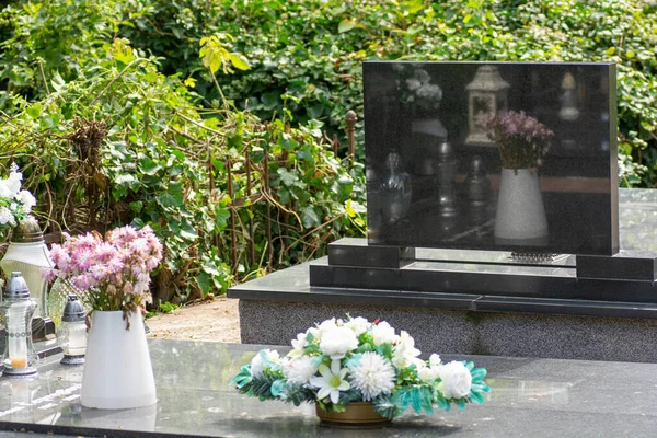 Mezarlıktaki siyah granit mezar taşının etrafındaki demir parmaklıkların yansıması..