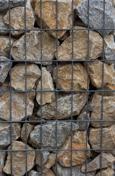 A fragment of wall made of wired cage filled with stones . Gabion wire mesh wall.