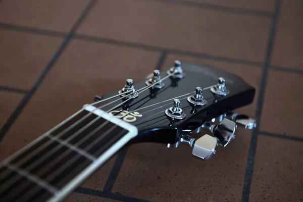 Headstock and tuners of beautiful black acoustic guitar lying on the brick floor closeup. Concept of vintage style.