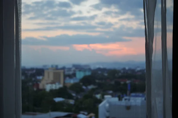 Fenêtre en verre avec coucher de soleil dans la vue sur la ville à l'extérieur de la chambre — Photo