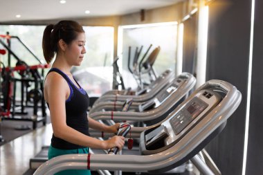koşu bandı kardiyo makine üzerinde çalışan asyalı kadın