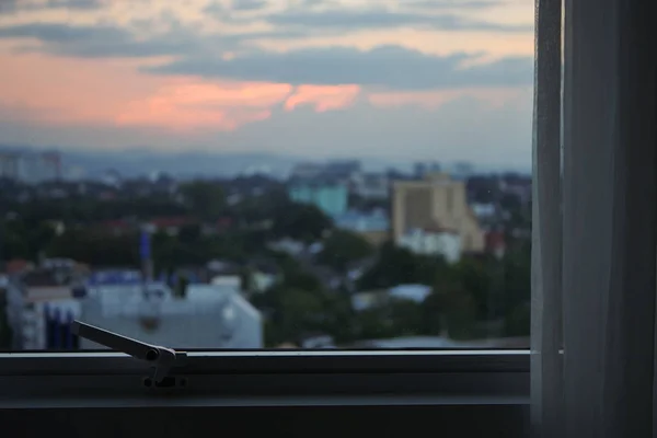 Oda dışında şehir görünümünde gün batımı gökyüzü ile cam pencere — Stok fotoğraf