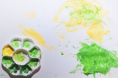 Bebek beyaz kağıda yeşil ve sarı suluboya boya boya kullanıyor. Renkli ve soyut bir hayal gücü var.