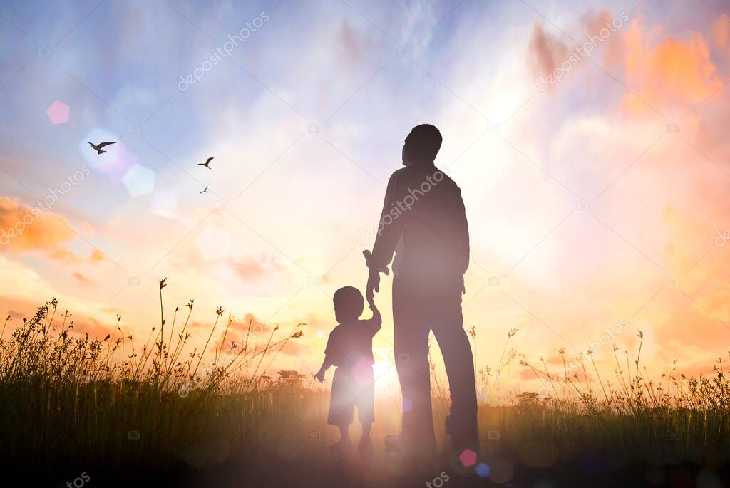 International migrants day concept: Silhouettes father and son holding hand in hand on meadow autumn sunset background
