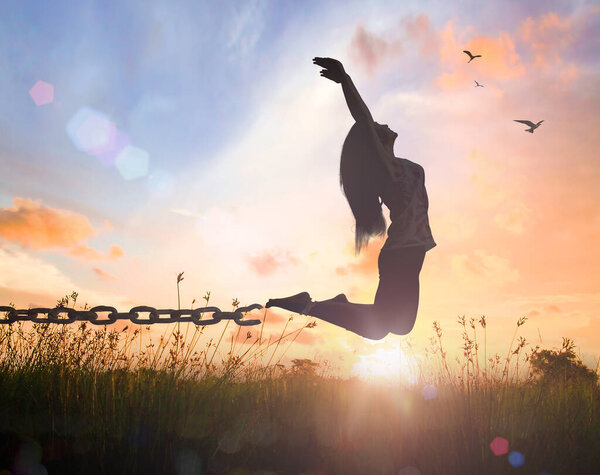 International day for the remembrance of the slave trade and its abolition concept: Silhouette of a girl jumping and broken chains at autumn sunset meadow with her hands raised