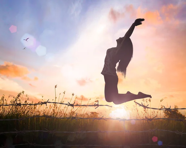 World mental health day concept: Silhouette of a girl jumping over broken barbed wire at meadow autumn sunset background