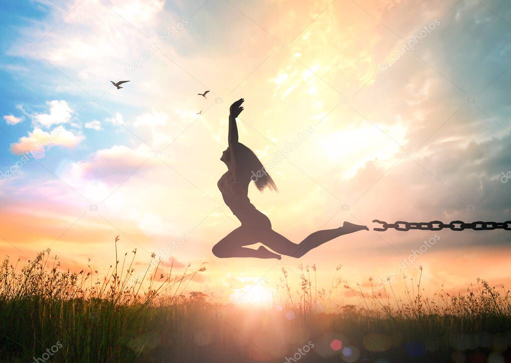 International day for the remembrance of the slave trade and its abolition concept: Silhouette of a girl jumping and broken chains at autumn sunset meadow with her hands raised