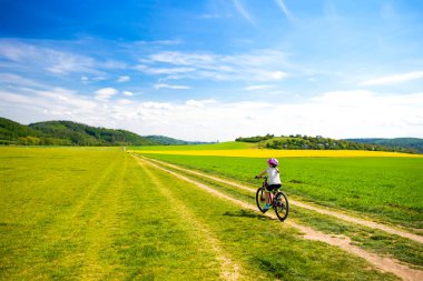 9 yaşındaki bir kız güneşli bir günde bisikletle tarlaları geçiyor, aile bisikletli tatilleri, yaz tatilleri. Özgürlük, aile, eğitim, eğlence ve spor kavramı.
