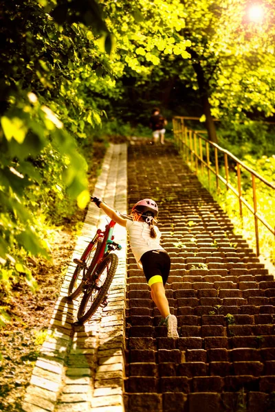 9 years girl bring up for the stairs her bicycle in the sunny day, family cyclo holidays, summertime. Freedom, family, education, recreation and sport concept.