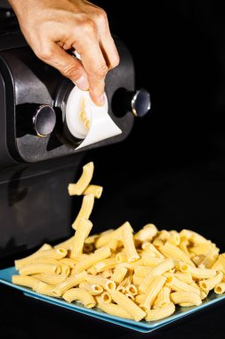 Makarna makinesinin yumurtalı makarnasıyla ev yapımı rigatoni hazırlıyorum. Siyah arkaplanda yakın plan fotoğrafı. Boşluğu kopyala.