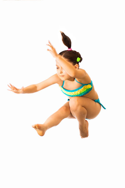 Little caucasian female 8 years old girl in cyan multicoloured swimmwear jumping on white background. Summertime, sport and recreation concept.