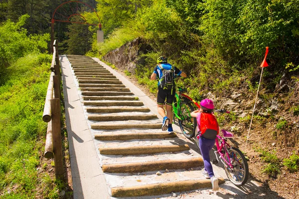 Father and daughter climb the steps with bicycle. Tandem, family cycling in Alpe Adria itinerary - Friuli-Venezia Giulia, Italy