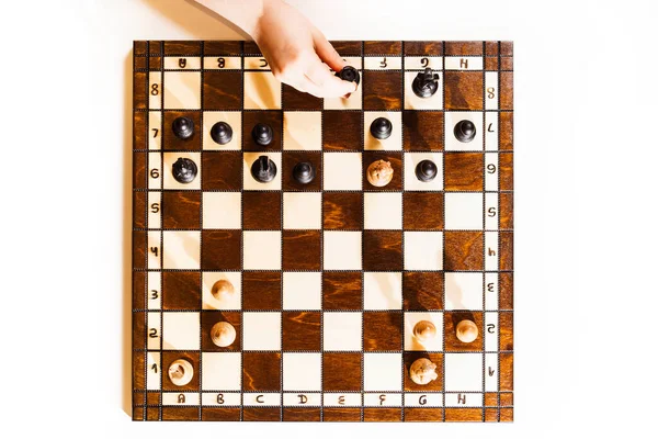 Chess board on white background. Little caucasian girl holding a black castle in the hand. The chess game. Top view.