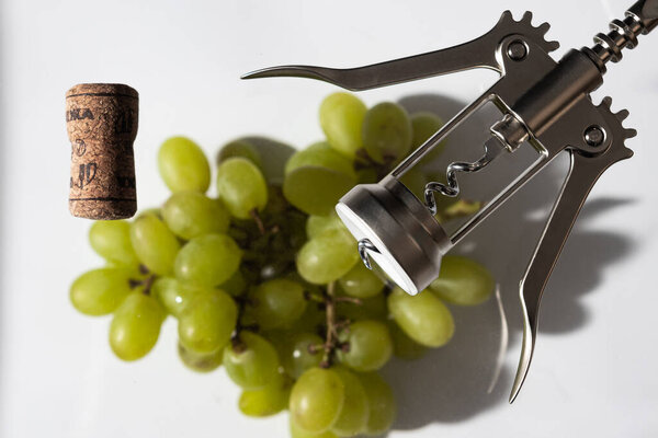зеленый виноград, пробка и штопор на белом фоне; студийная фотография с мягким освещением
