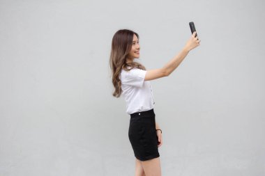 Taylandlı yetişkin öğrenci üniformasının portresi. Güzel kız akıllı telefonuyla selfie çekiyor.