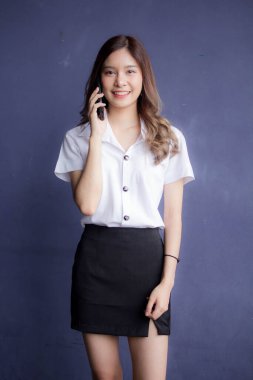 Taylandlı yetişkin öğrenci üniformasının portresi. Güzel bir kız akıllı telefondan arıyor.